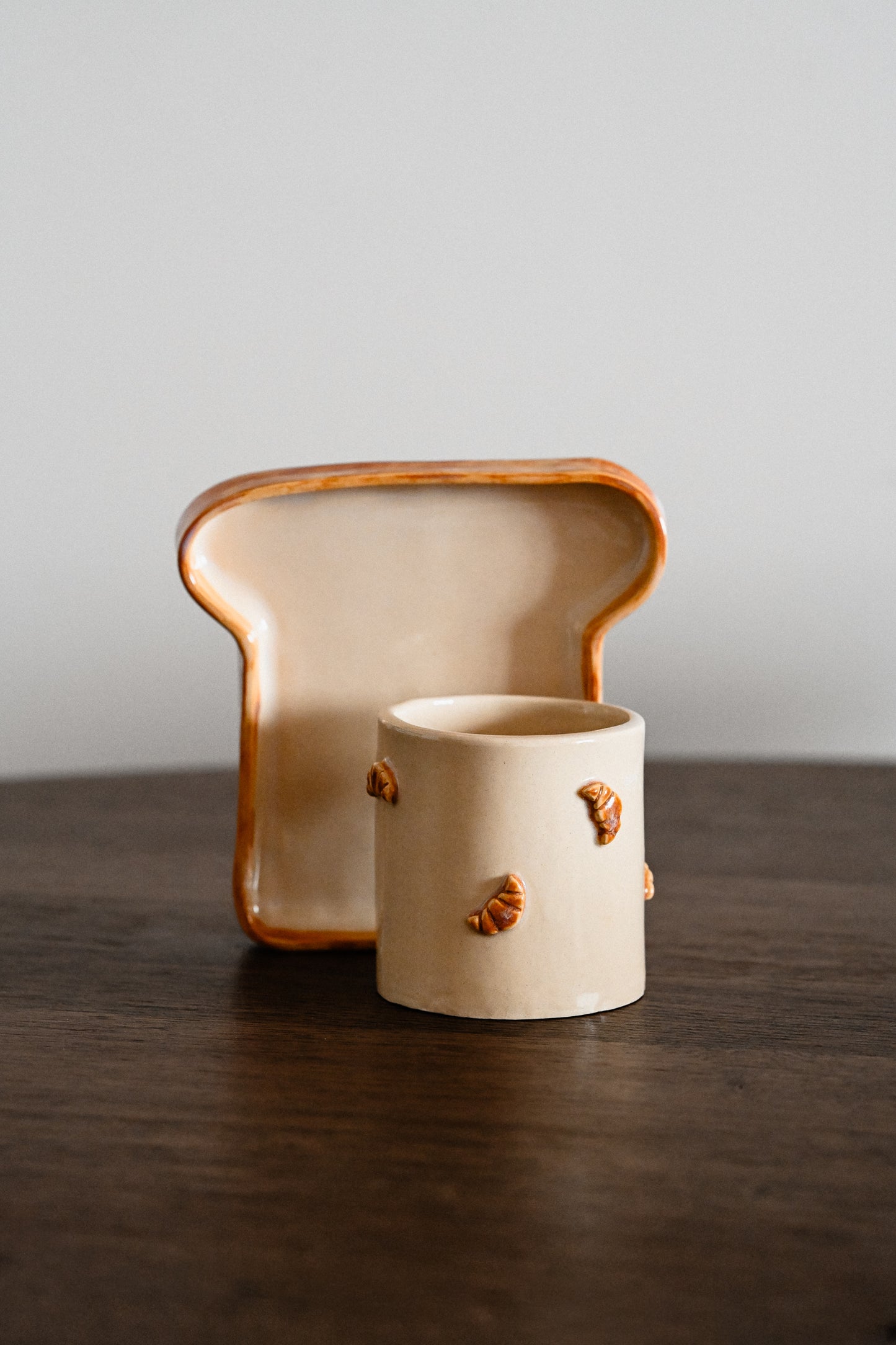 Hand-built ceramic breakfast set with a croissant-decorated mug and a toast-shaped plate on a wooden table.